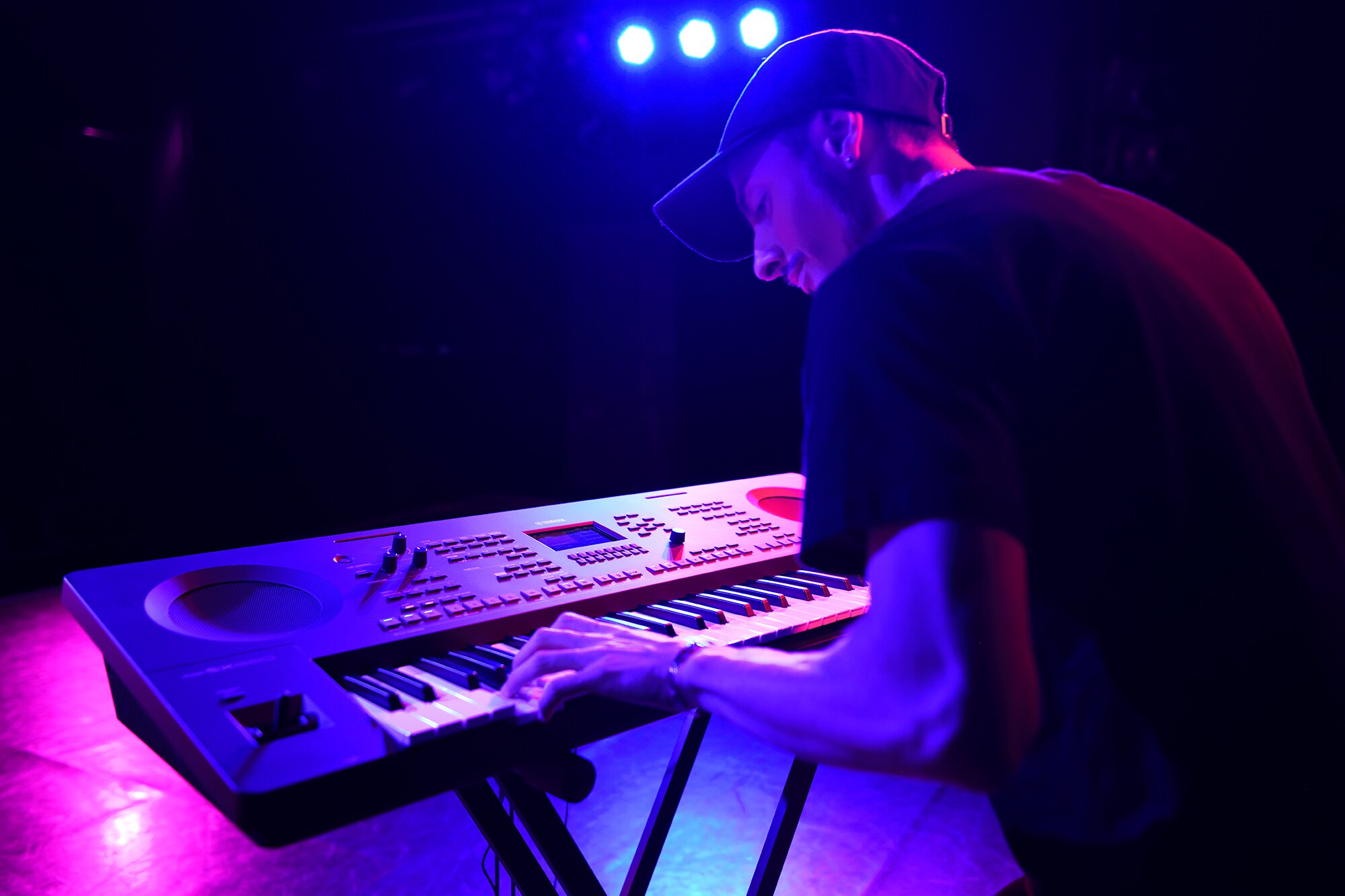 Iemand die een Yamaha arranger workstation bespeelt op een statief onder podiumverlichting
