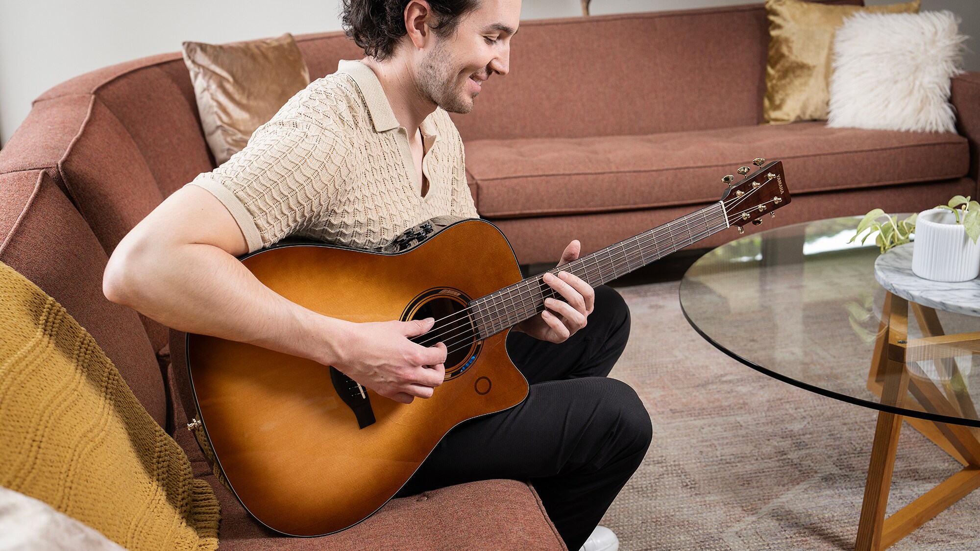 Een man zittend op een bank in de woonkamer bespeelt een TAG3 C akoestische gitaar