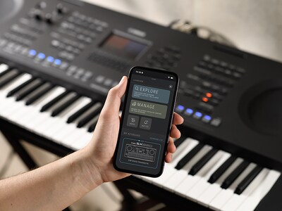 PSR-SX620 en een hand die een smartphone vasthoudt met het scherm van de officiële Yamaha-app 'Expansion Explorer'.