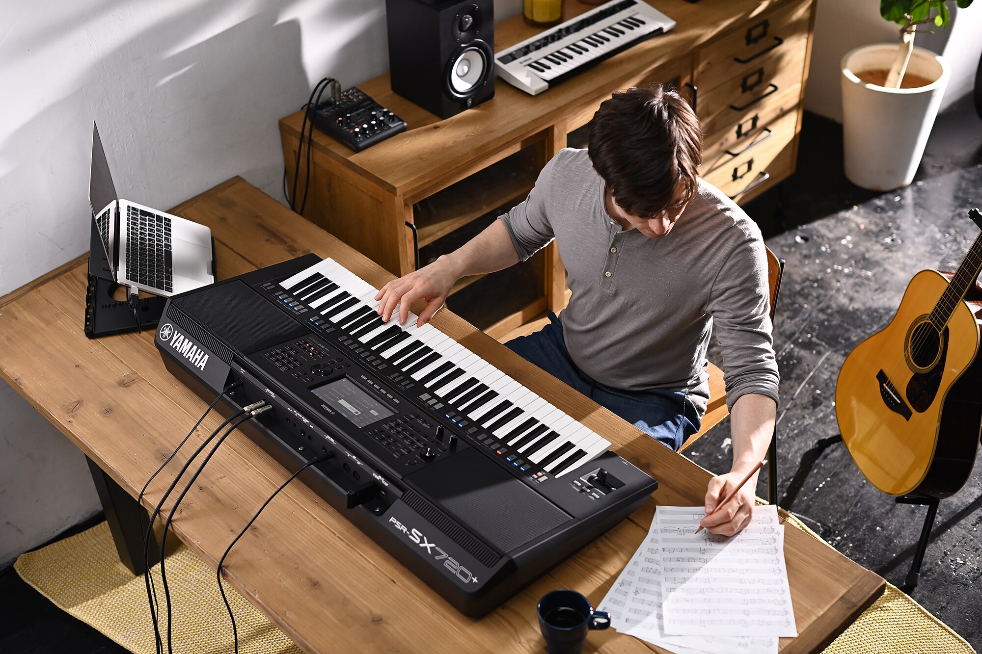 Foto van iemand die op bladmuziek schrijft terwijl diegene op de Yamaha Arranger Workstation PSR-SX720+ speelt