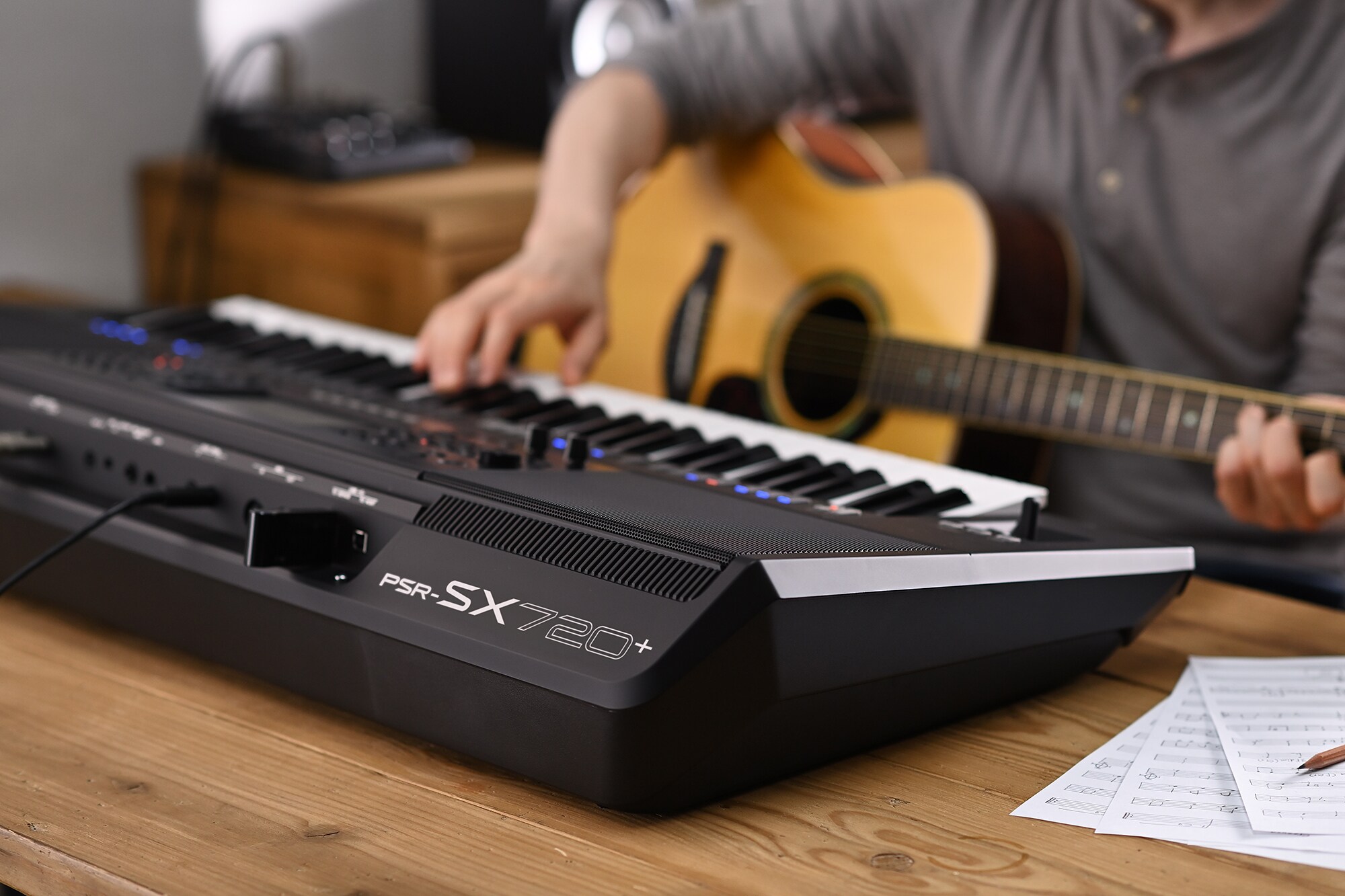 Foto van iemand die op de Yamaha Arranger Workstation PSR-SX720+ speelt terwijl deze een gitaar vasthoudt