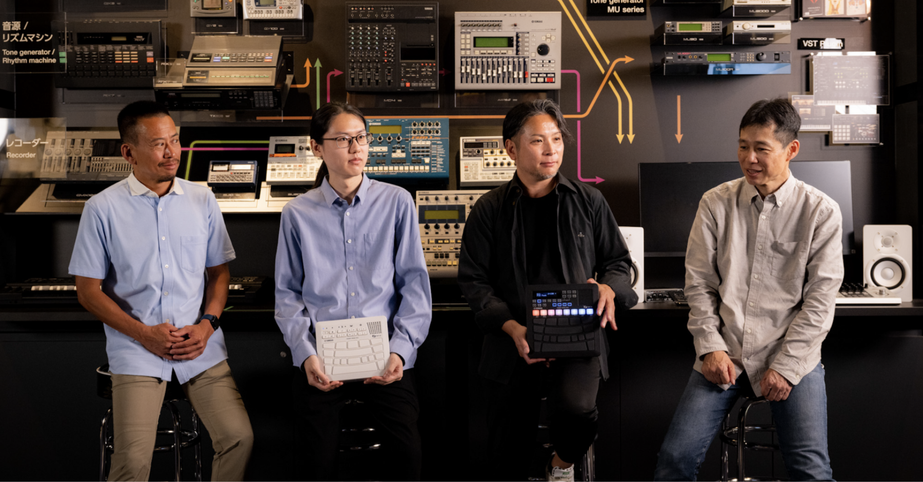 Four members of the Sound Creator Team lined up in front of successive generations of Yamaha’s DTM equipment