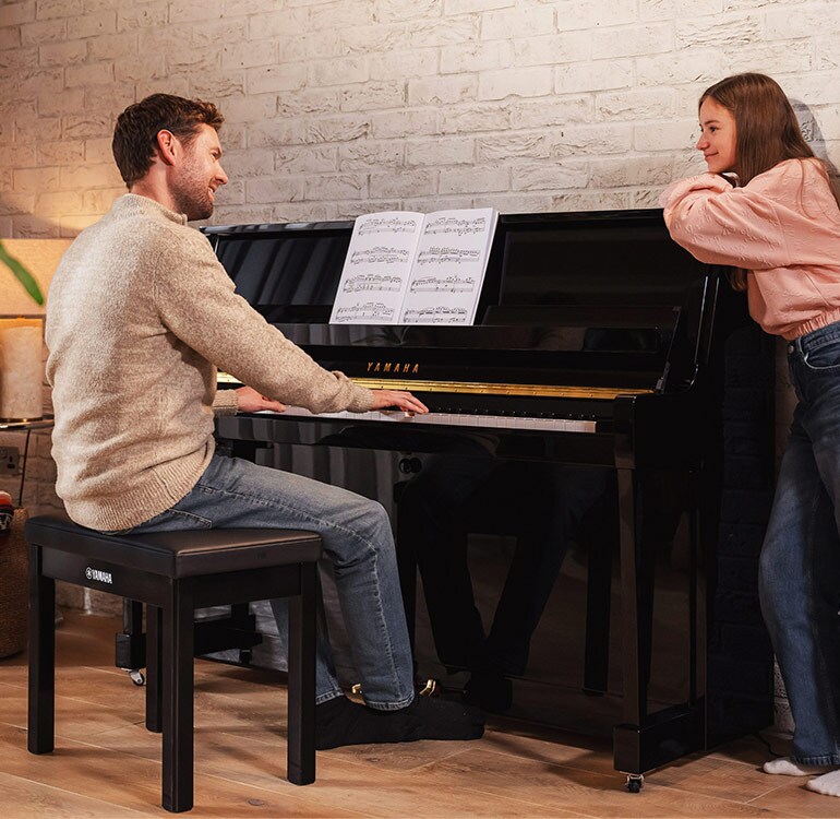 Een moeder en dochter spelen met plezier op een staande piano uit de B-serie