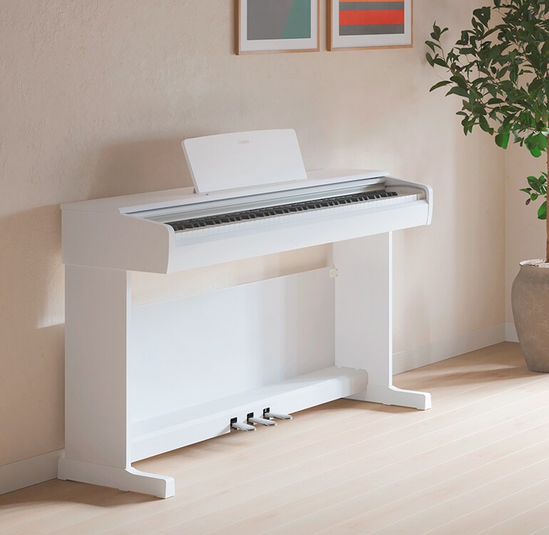 Een woonkamer met een witte ARIUS-piano, kamerplanten en een bank, harmonieus geïntegreerd in het interieur