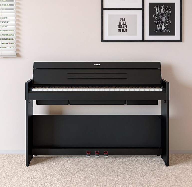 Een woonkamer met een zwarte ARIUS-piano geplaatst naast wandplanken waarop lampen en een diffuser staan, harmonieus geïntegreerd in het interieur.