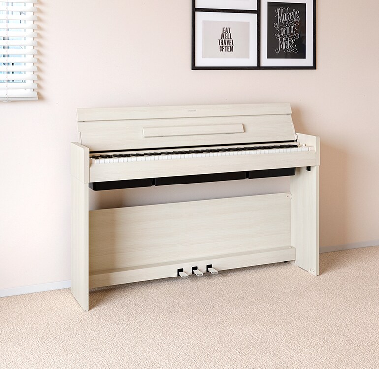 Een woonkamer met een wit berken ARIUS-piano geplaatst naast wandplanken waarop lampen en een diffuser staan, harmonieus geïntegreerd in het interieur.