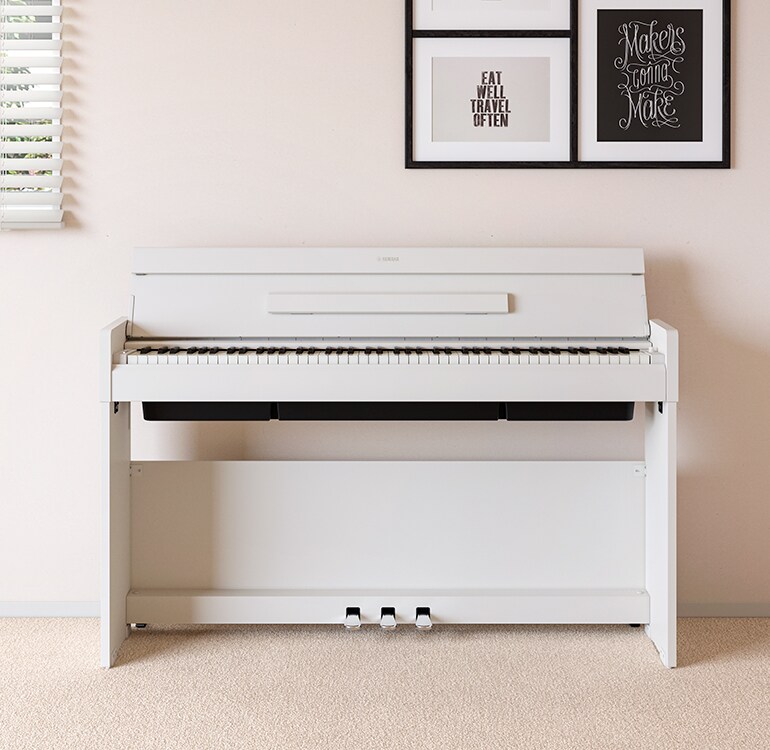 Een woonkamer met een witte ARIUS-piano geplaatst naast wandplanken waarop lampen en een diffuser staan, harmonieus geïntegreerd in het interieur.