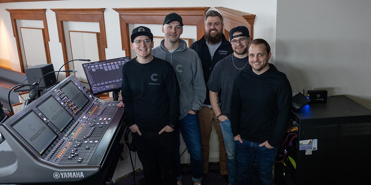 Members of the Christ Community Chapel audio team standing beside a Yamaha RIVAGE PM mixing console.